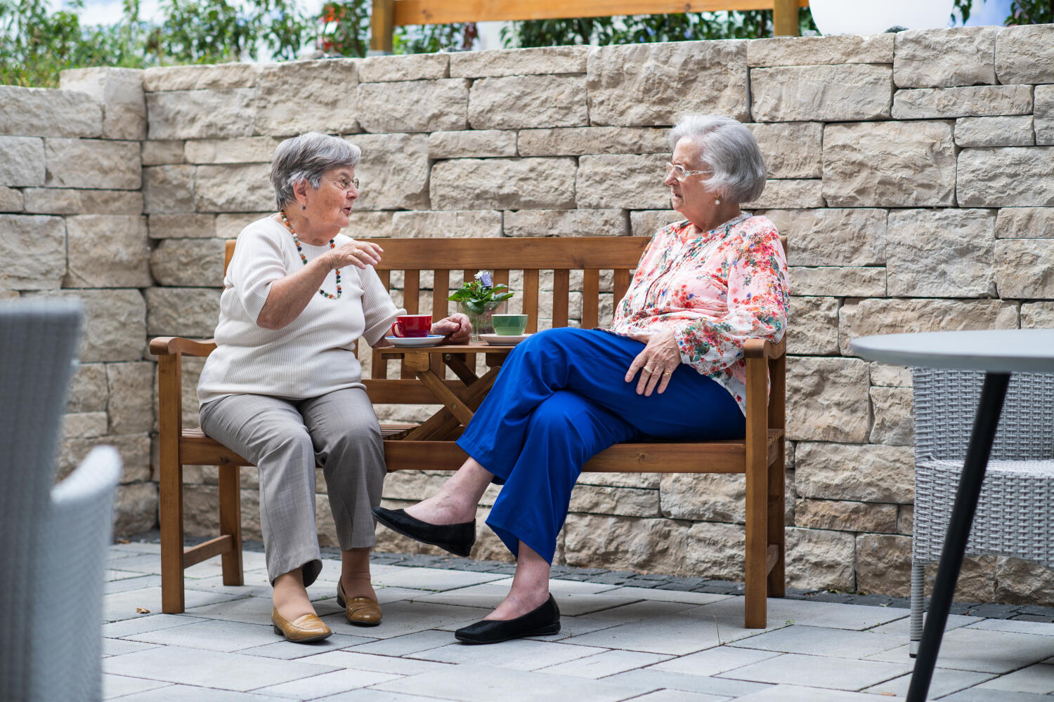In einer windgeschützten Ecke aus großen, gelben Quadersteinen sitzen zwei älterer Damen auf einer Bank mit eingebautem Tisch beim "Kaffeklatsch".