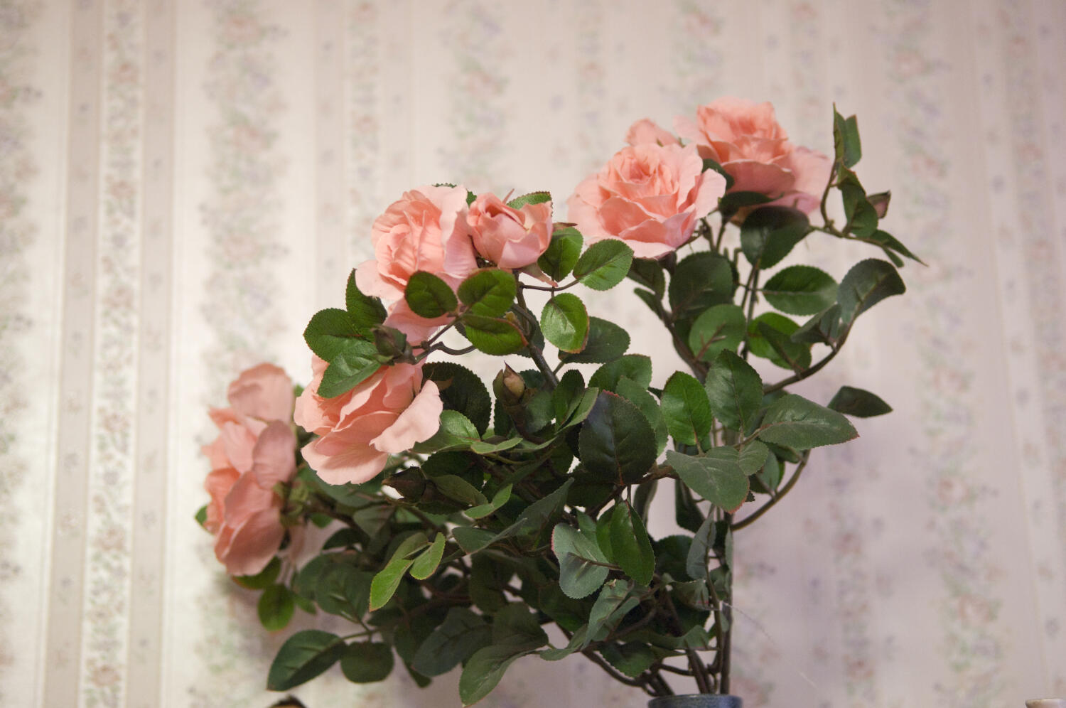 In einer grünlichen Vase ein kleiner Strauß rosaroter Rosen mit grünen, kräftigen Blättern.