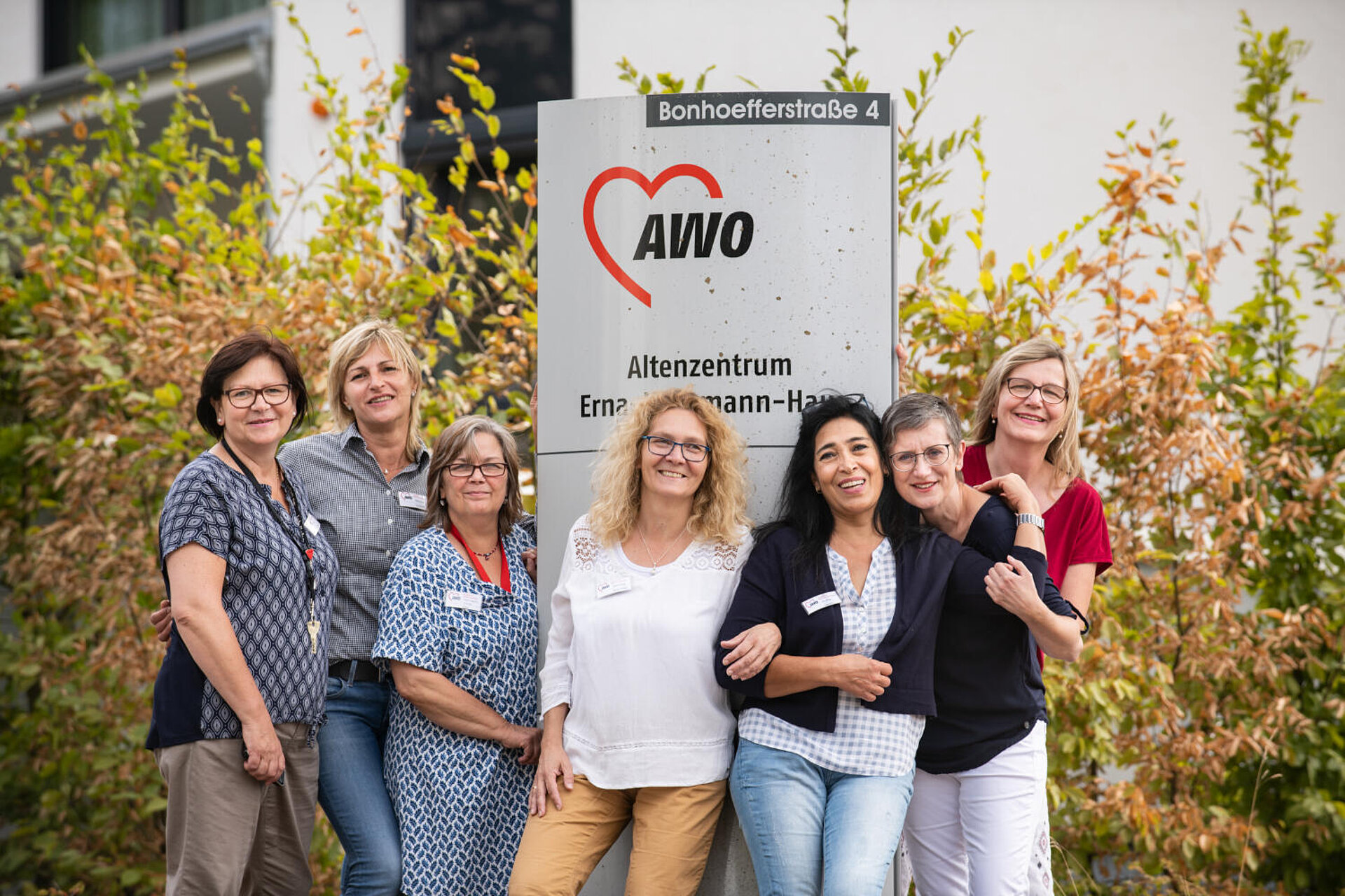Das lächelnde Team - 6 Frauen - präsentiert sich vor einem großen AWO-Logo. Es sieht wie eine Einladung aus.