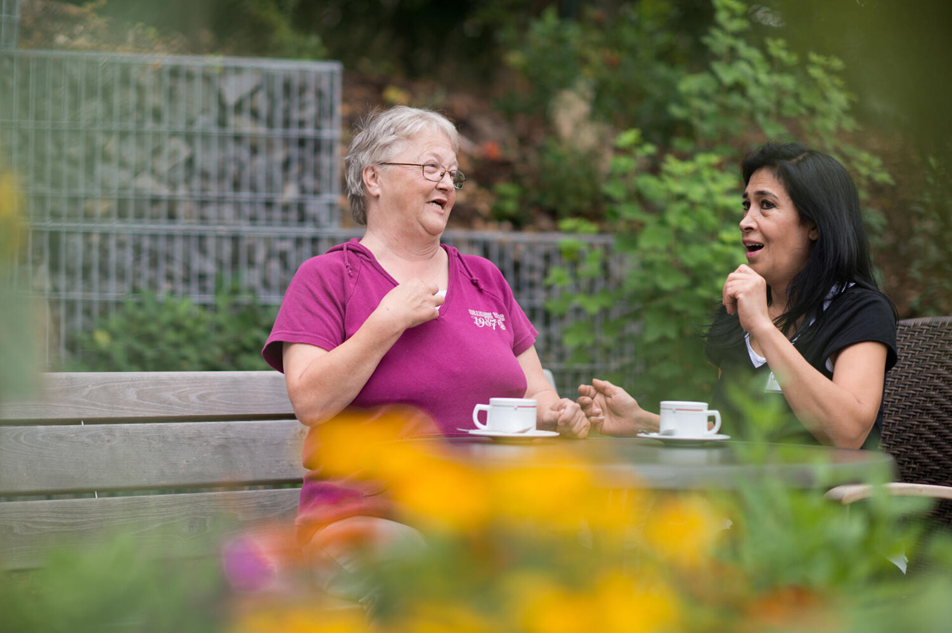 "Kaffeeklatsch" zweier Damen im Garten, de sichtbar Freude macht.