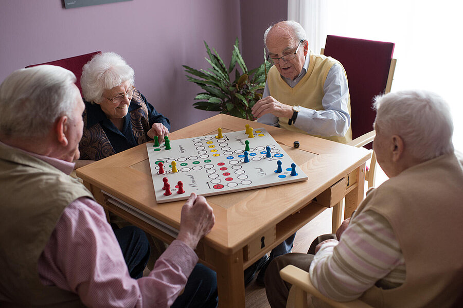 Vier Bewohner spielen an einem viereckigen Tisch vergnügt "Mensch ärgere Dich nicht ".